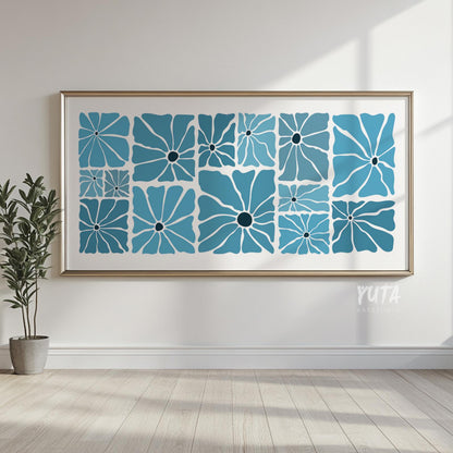 Mid century blue floral artwork in a thin metallic frame, hung on a sunlit white wall above wood flooring.