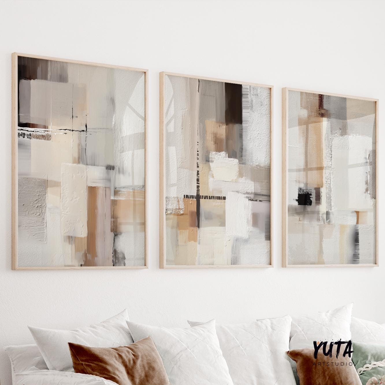 Three framed abstract prints with neutral geometric brushwork displayed above a white sofa in daylight