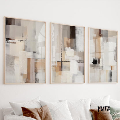 Three framed abstract prints with neutral geometric brushwork displayed above a white sofa in daylight