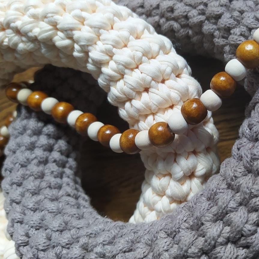 Close up of handmade gray and beige cotton decor showing woven texture, natural wooden beads and braided details