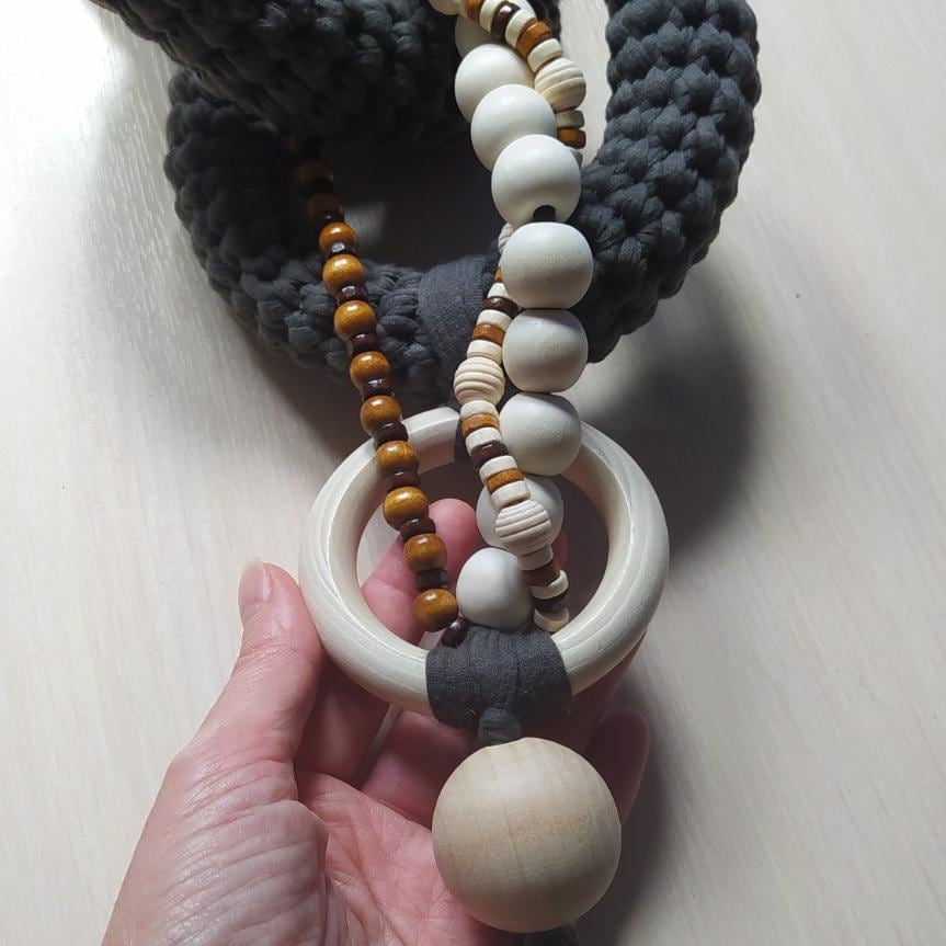 Close up of handmade decorative chain showing textured gray fiber links and wooden beads
