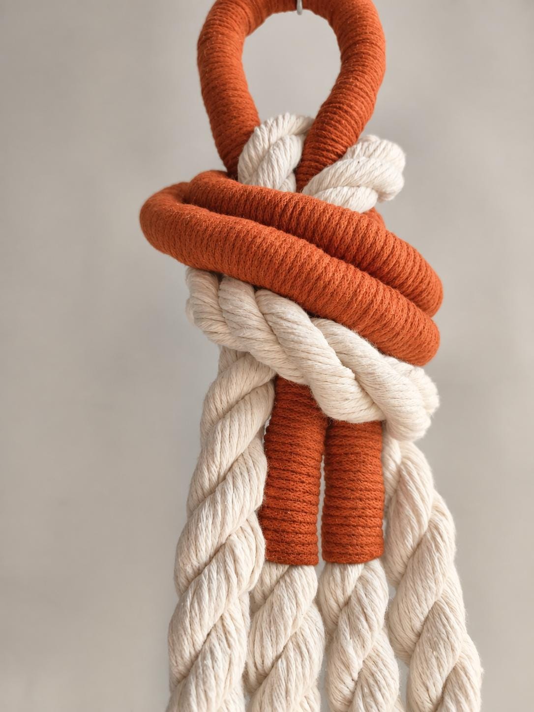 Close up of cream rope wall hanging with orange wrapped accent details