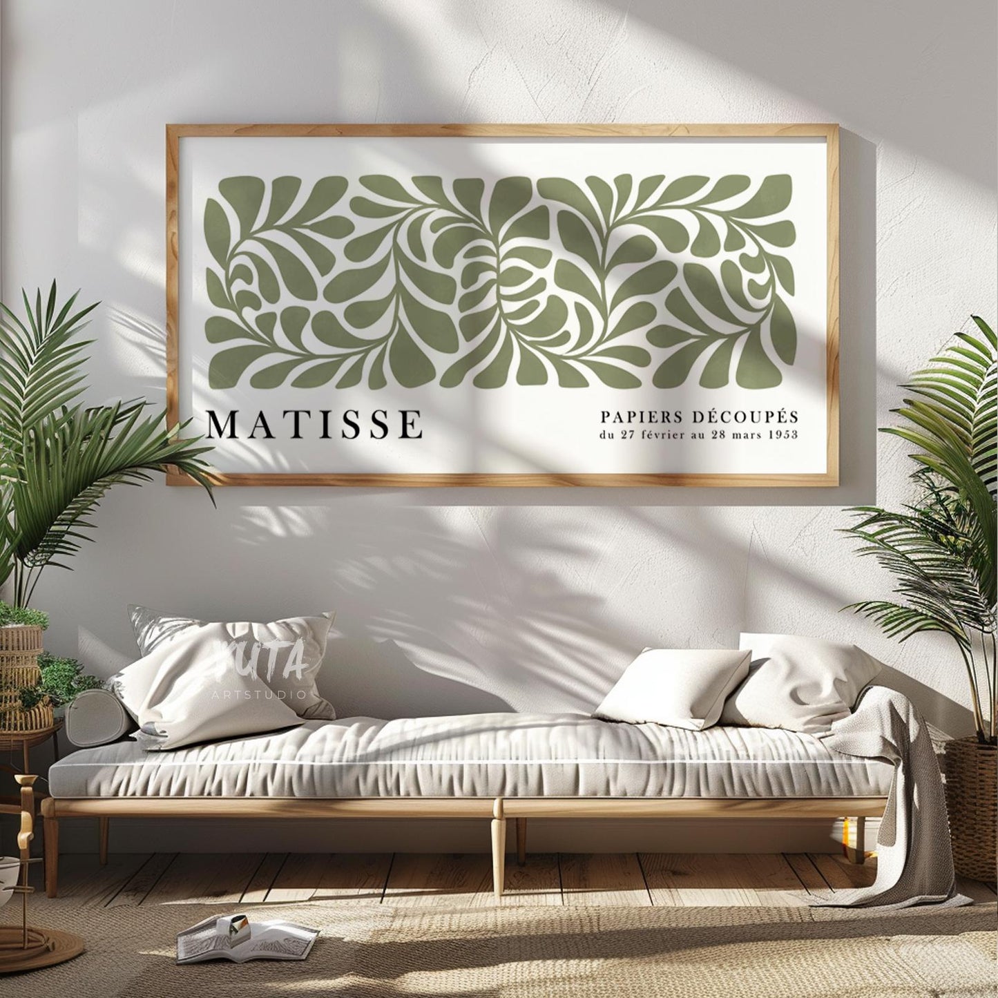 Sage green abstract Matisse-inspired print in light wood frame above a daybed with plants