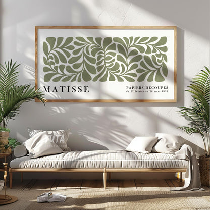 Sage green abstract Matisse-inspired print in light wood frame above a daybed with plants