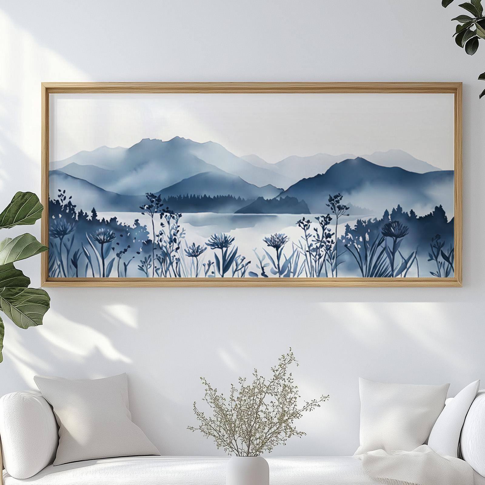 Navy blue mountain lake landscape print in a light wood frame above a white sofa
