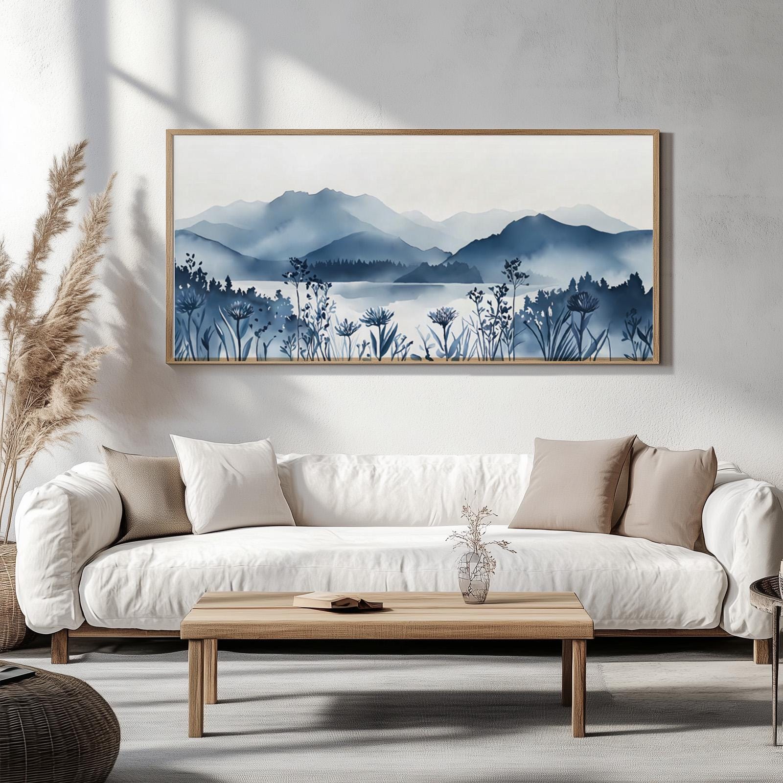 Wide navy blue mountain lake artwork in a natural wood frame above a white sofa with pampas grass