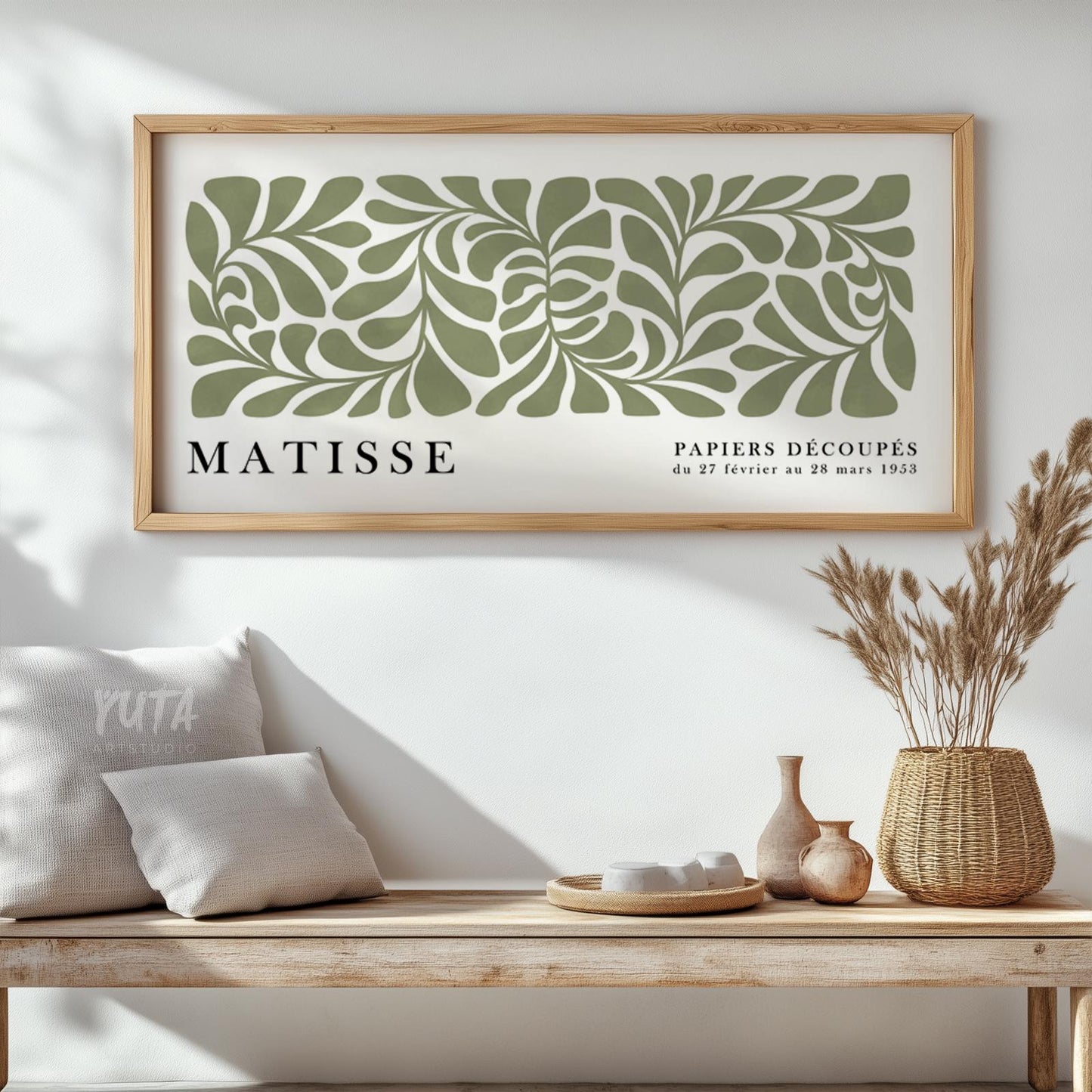 Abstract sage green leaf cut-out artwork in a light wood frame above a rustic bench