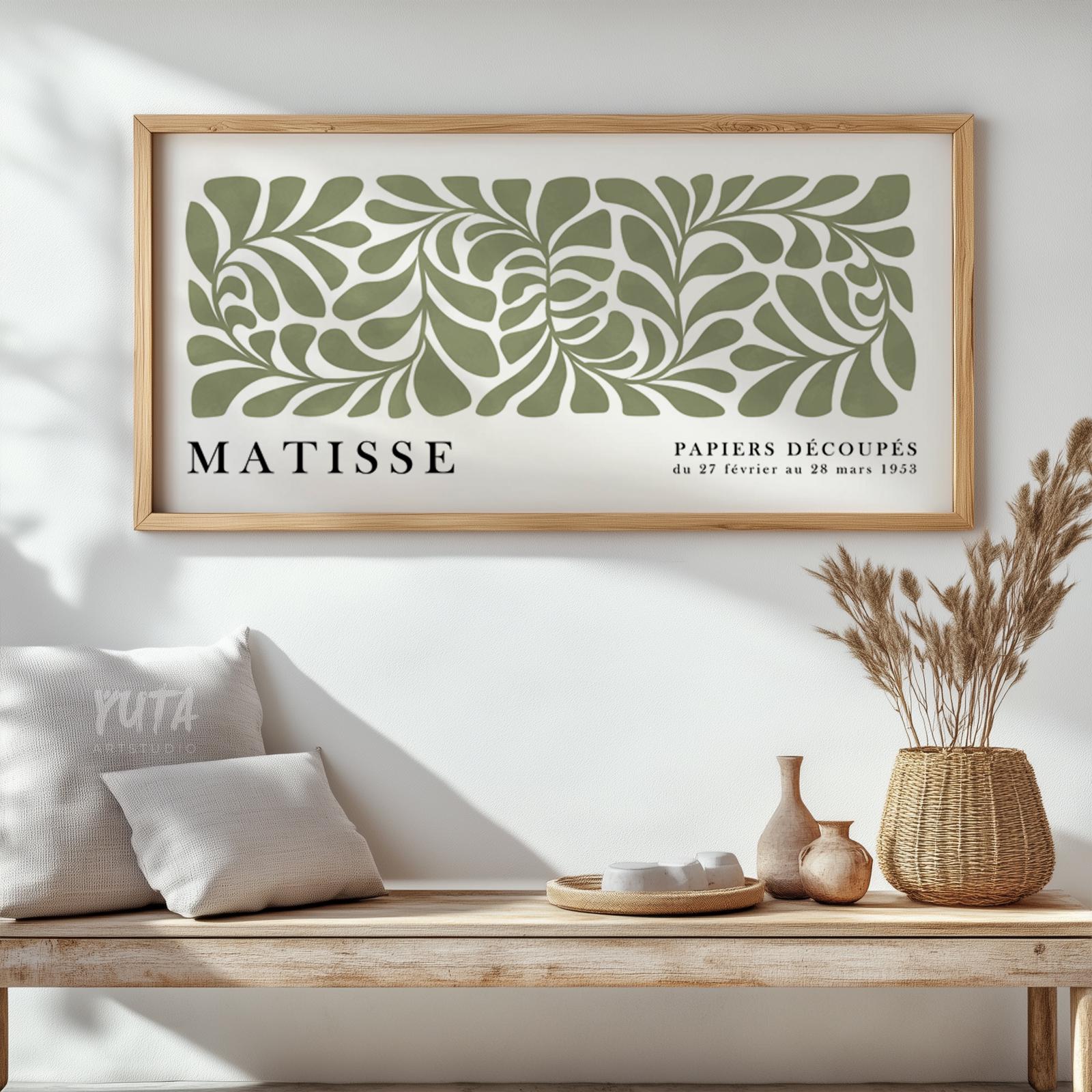 Abstract sage green leaf cut-out artwork in a light wood frame above a rustic bench