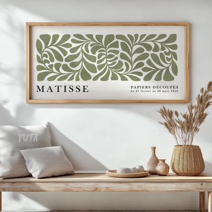 Abstract sage green leaf cut-out artwork in a light wood frame above a rustic bench