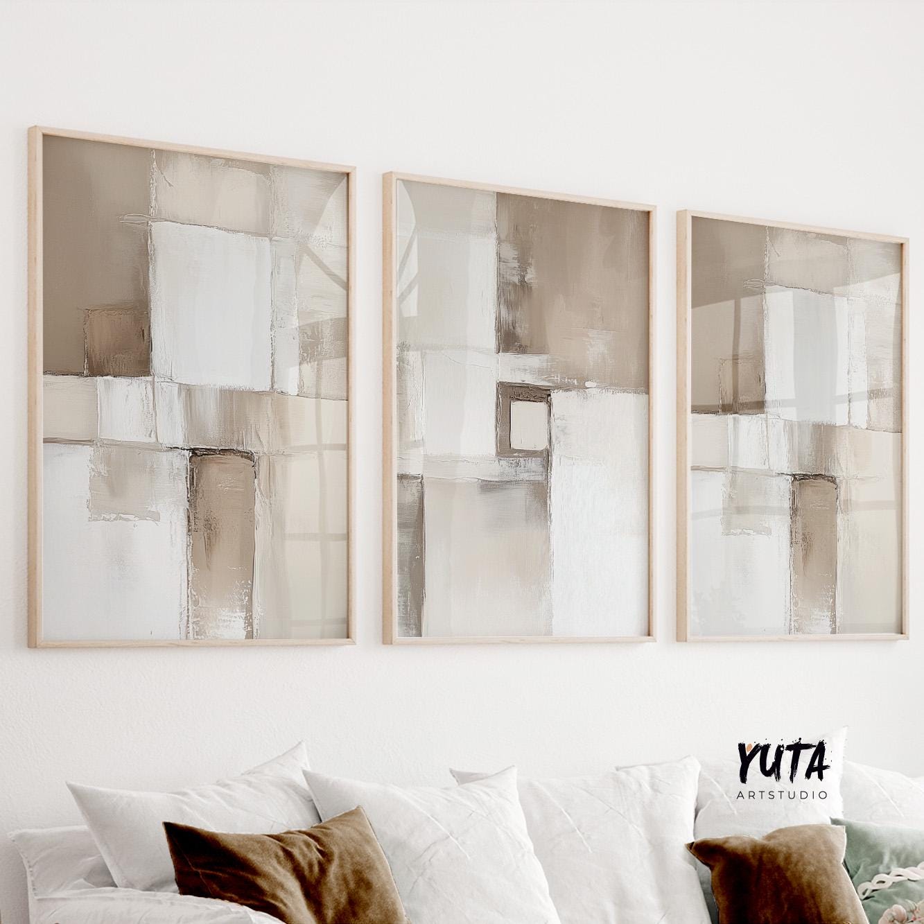 Neutral abstract triptych in light wood frames displayed above a white sofa with cushions