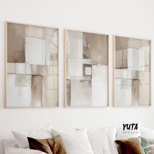 Neutral abstract triptych in light wood frames displayed above a white sofa with cushions
