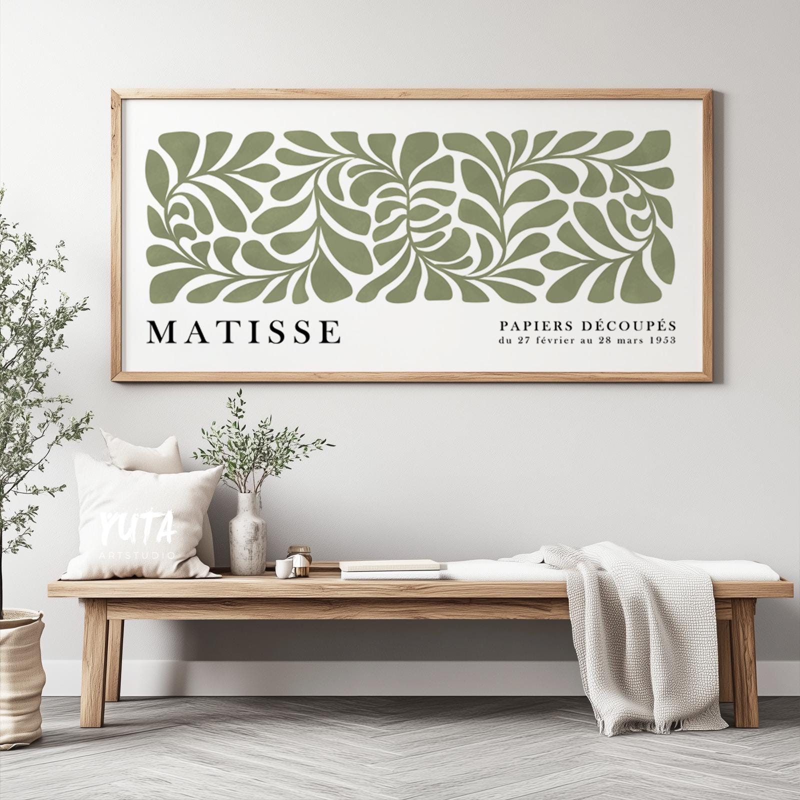 Framed sage green abstract cut-out print styled above a wooden bench with decor accents