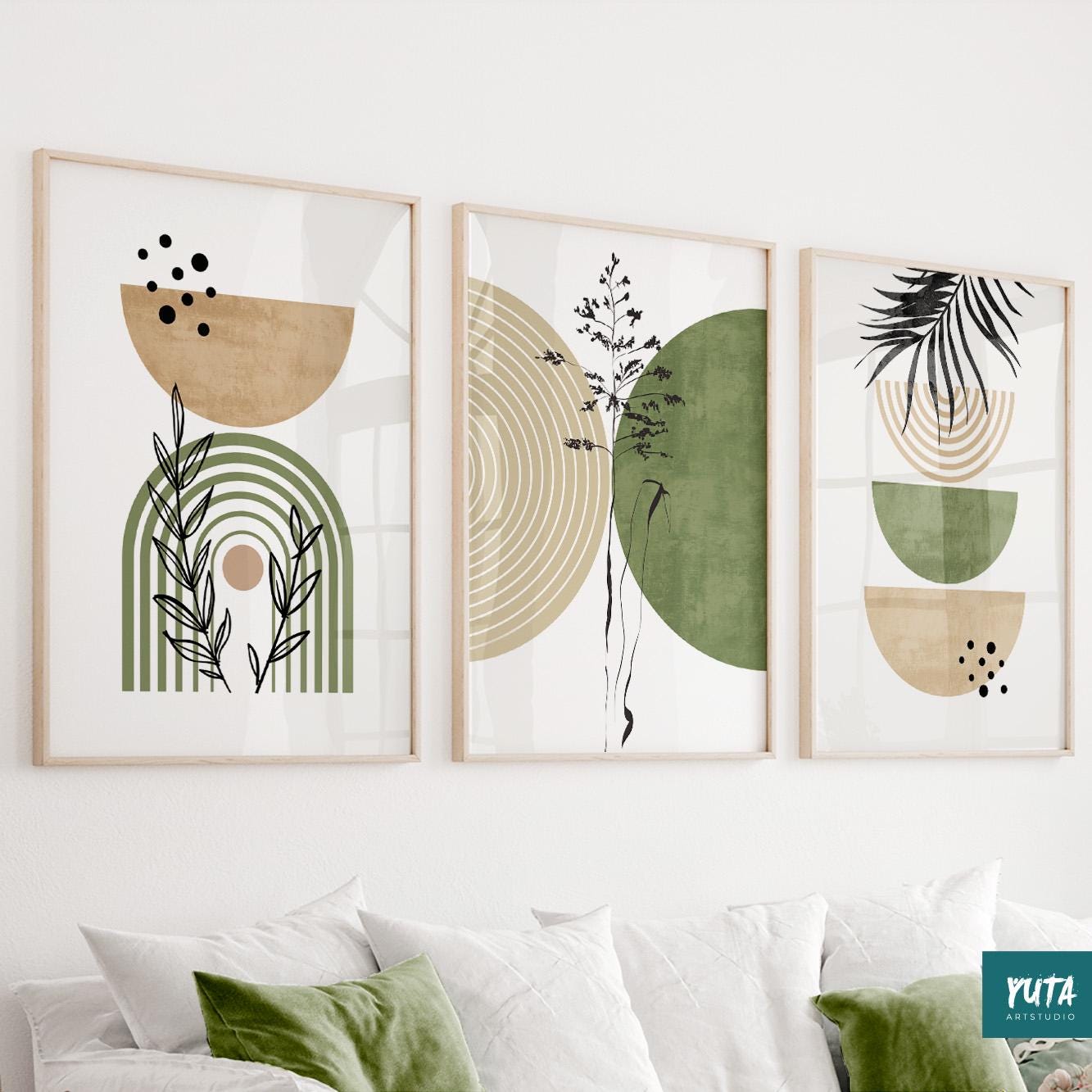 Three abstract boho prints in light wood frames arranged above a white sofa.