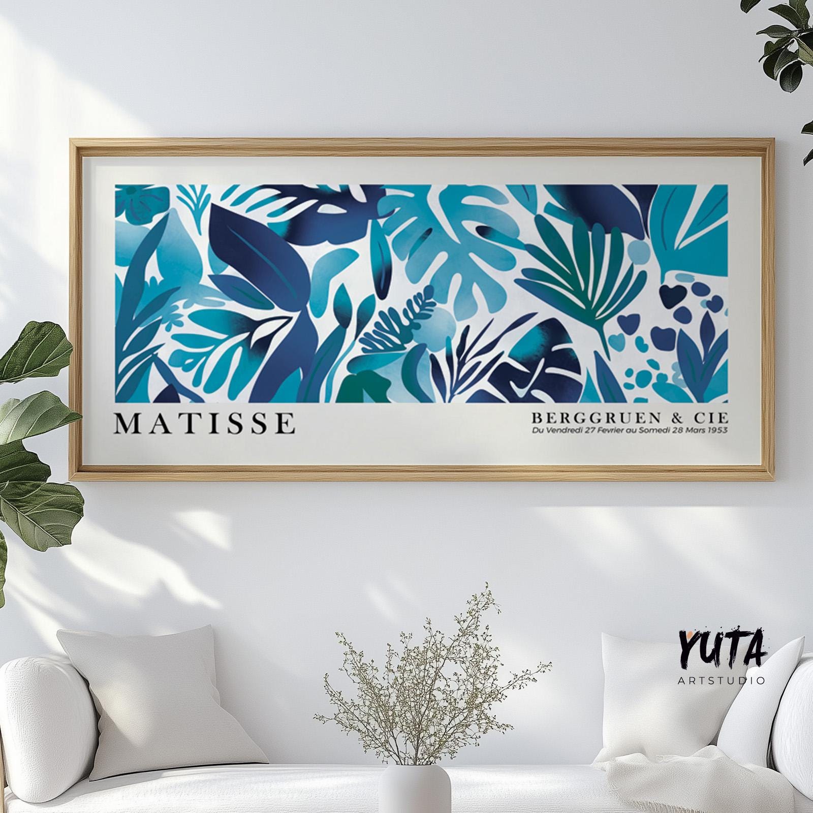 Framed blue tropical leaves print in Matisse style on white wall above a sofa