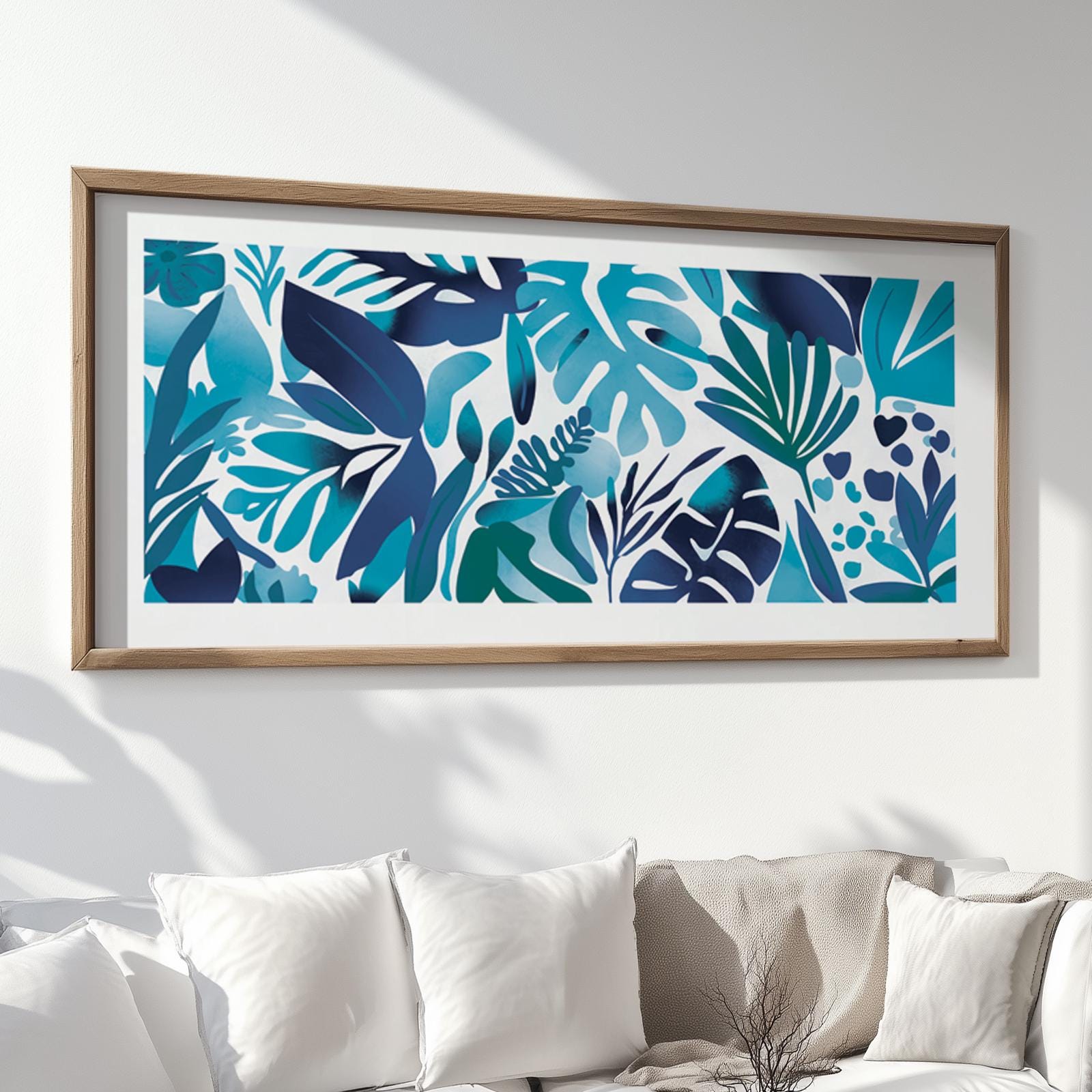Framed blue tropical leaves artwork displayed above a white sofa in natural sunlight
