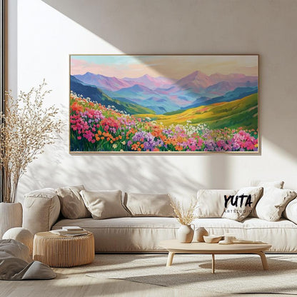 Large framed mountain landscape with vibrant wildflowers displayed above a beige sofa in sunlight