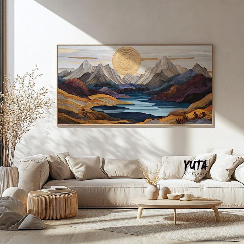 Framed pastel mountain landscape art centered above a cream sofa in a sunlit room
