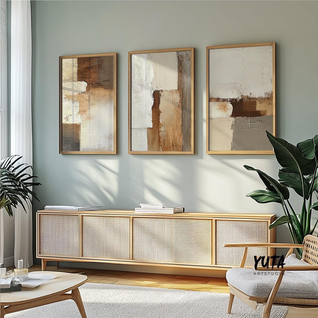 Three framed abstract prints in earth tones hung above a console with books and leafy plants