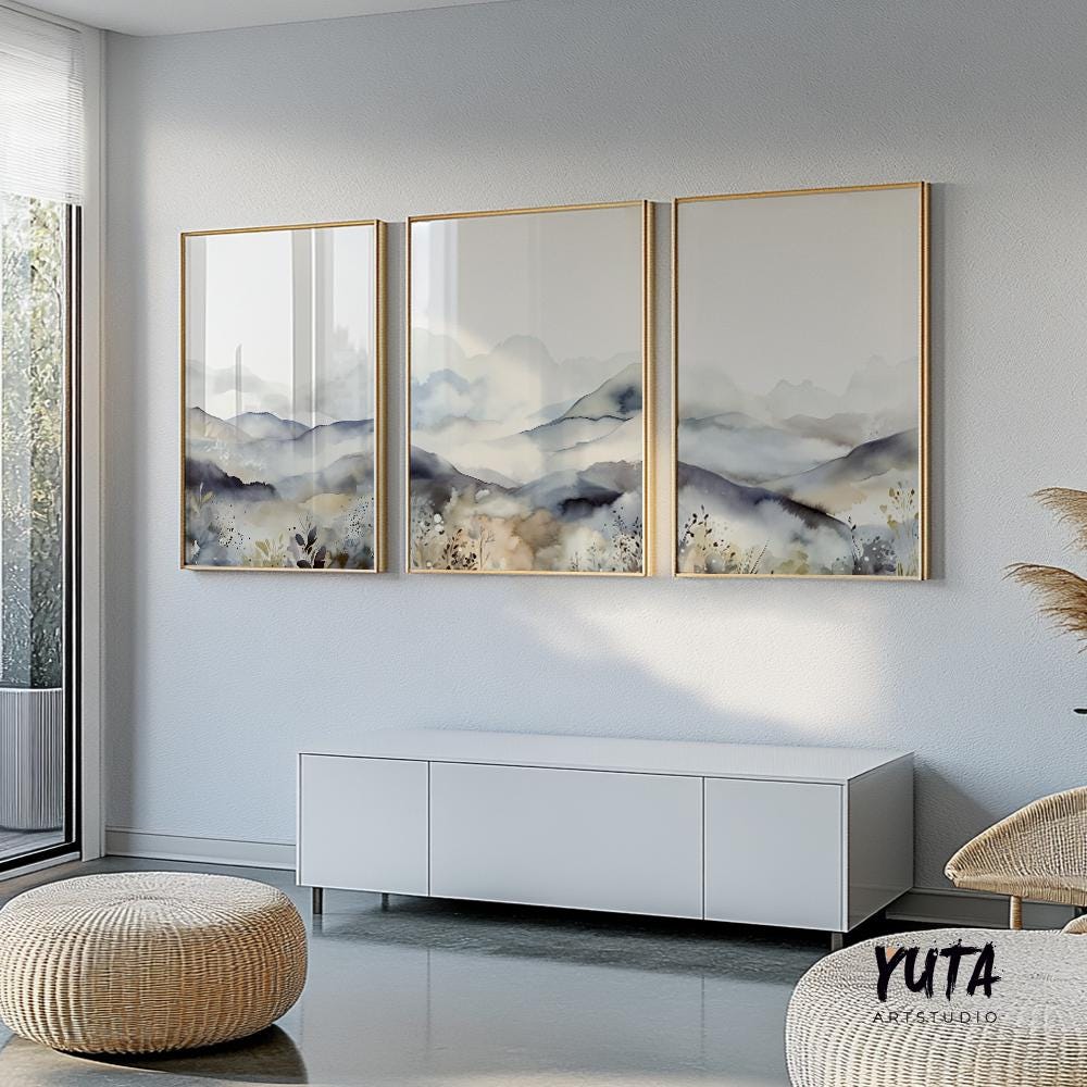 Three minimalist mountain prints in gold frames above a white cabinet with books and plants