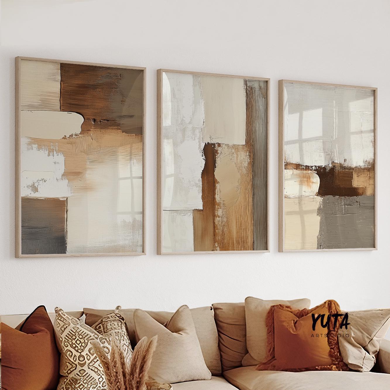 Three abstract neutral earth tone prints in light wood frames arranged over a beige sofa