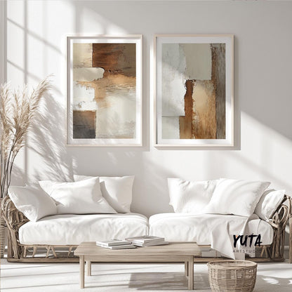 Beige and brown abstract art pair in light wood frames above a sofa with dried pampas grass and books.